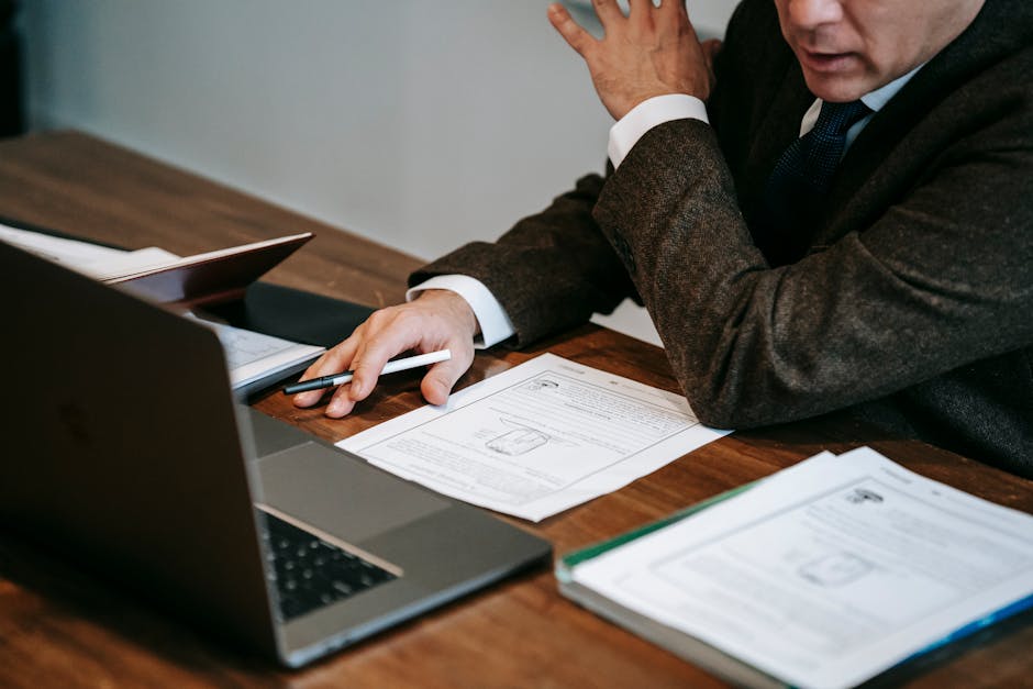 A business professional in formal attire analyzing documents and using a laptop for work indoors.