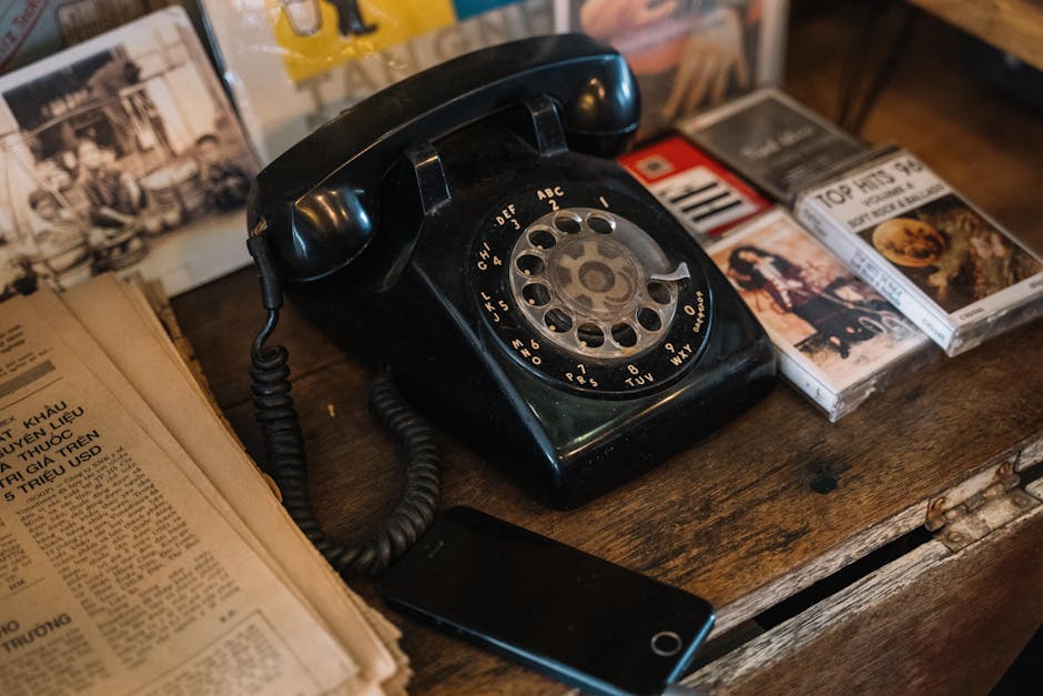A nostalgic scene of a classic rotary phone surrounded by tapes and newspapers on a wooden surface.